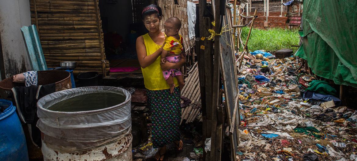 在缅甸仰光，一名妇女抱着六个月大的儿子，站在他们临时搭建的小房子前。