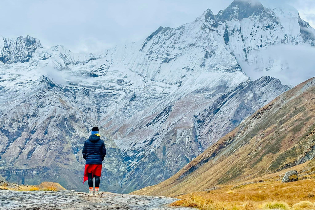 Uma pessoa está em um afloramento rochoso olhando para uma vasta cordilheira coberta de neve no Nepal.