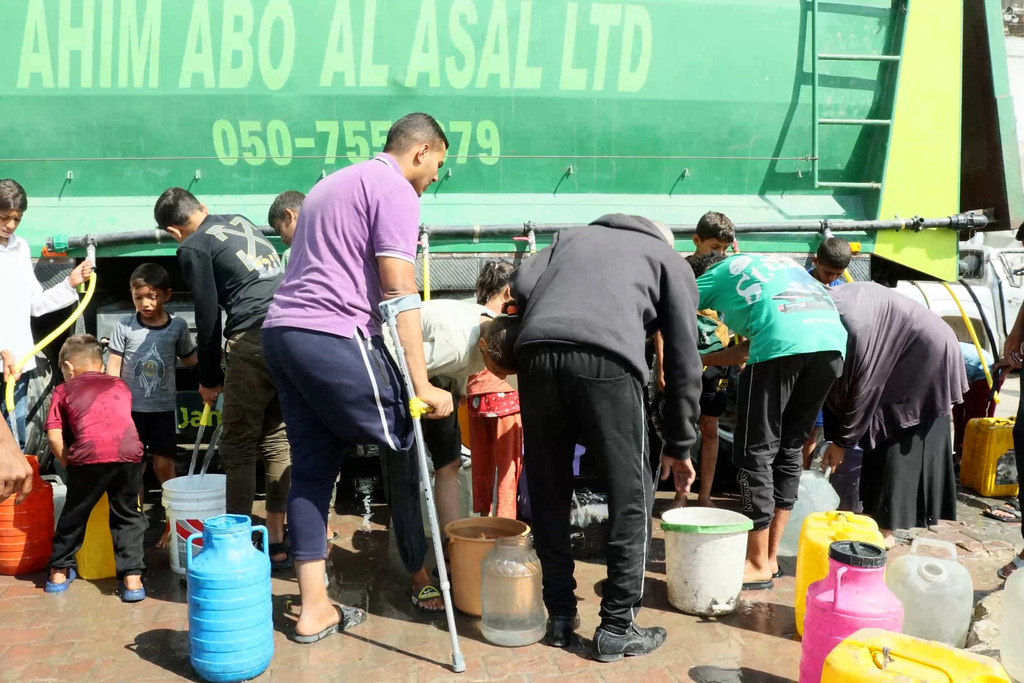 Des personnes se rassemblent pour remplir des récipients avec de l'eau potable provenant d'un camion de distribution du PNUD à Gaza.