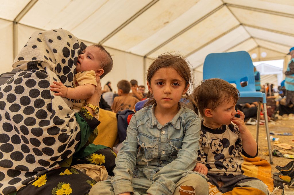 Una joven afgana se sienta con sus hermanos y madre dentro de una gran carpa en el punto fronterizo de Islam-Qala en Afganistán. La familia, originaria de Badakhshan, regresó de Irán después de años de migración indocumentada debido a dificultades económicas. Ahora no tienen refugio y luchan por sobrevivir, con necesidades urgentes de pañales, vivienda y apoyo financiero.