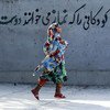 Garota vestindo hijab no Irã passa correndo por um mural que diz, em persa, “Deus ama as crianças que dizem suas ‘namaz’ [orações]”. (Arquivo)