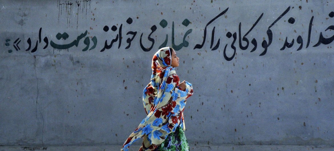 Garota vestindo hijab no Irã passa correndo por um mural que diz, em persa, “Deus ama as crianças que dizem suas ‘namaz’ [orações]”. (Arquivo)