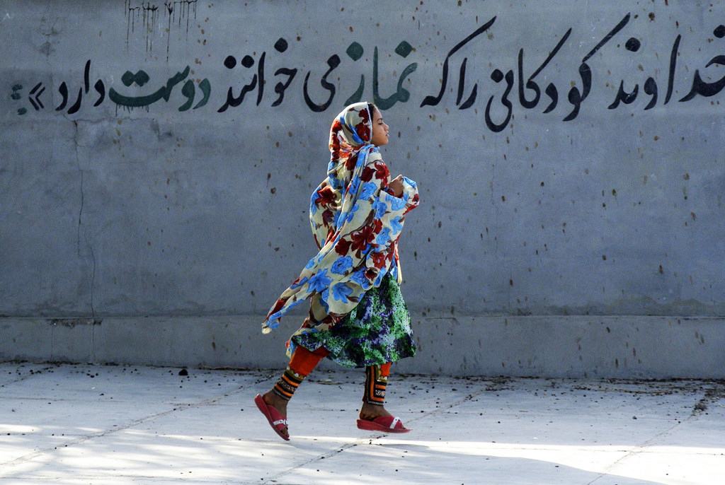 من الأرشيف: فتاة ترتدي حجابها في إيران تسير بقرب لوحة جدارية تقول باللغة الفارسية "إن الله يحب الأطفال الذين يصلون". 