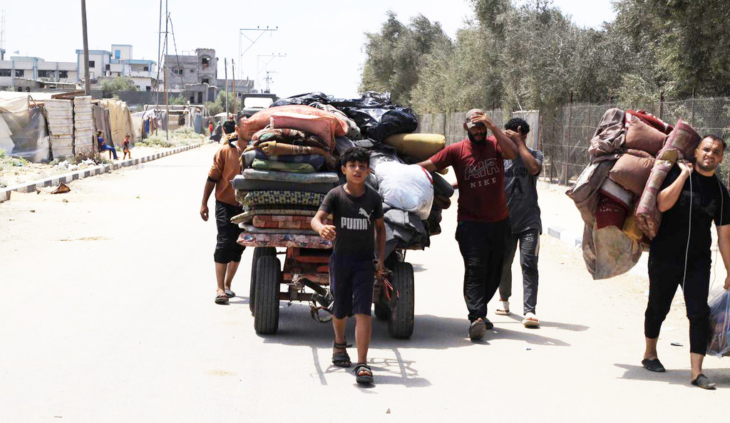 Des civils palestiniens, dont un jeune garçon, marchent le long d'une route, portant de gros ballots de leurs affaires, certains poussant une charrette à bras, lors d'une évacuation de Gaza.