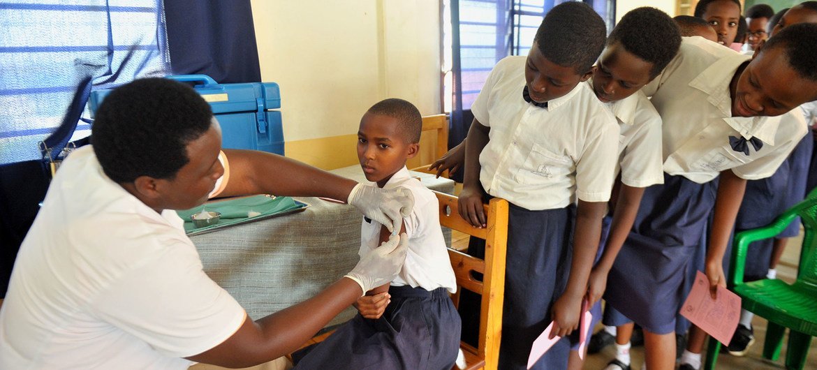 रवाण्डा में एक युवा लड़की को एचपीवी की वैक्सीन दी जा रहीहै और अन्य स्कूली छात्राएँ भी अपनी बारी का उत्सुकता और घबराहट में इन्तज़ार कर रही हैं.