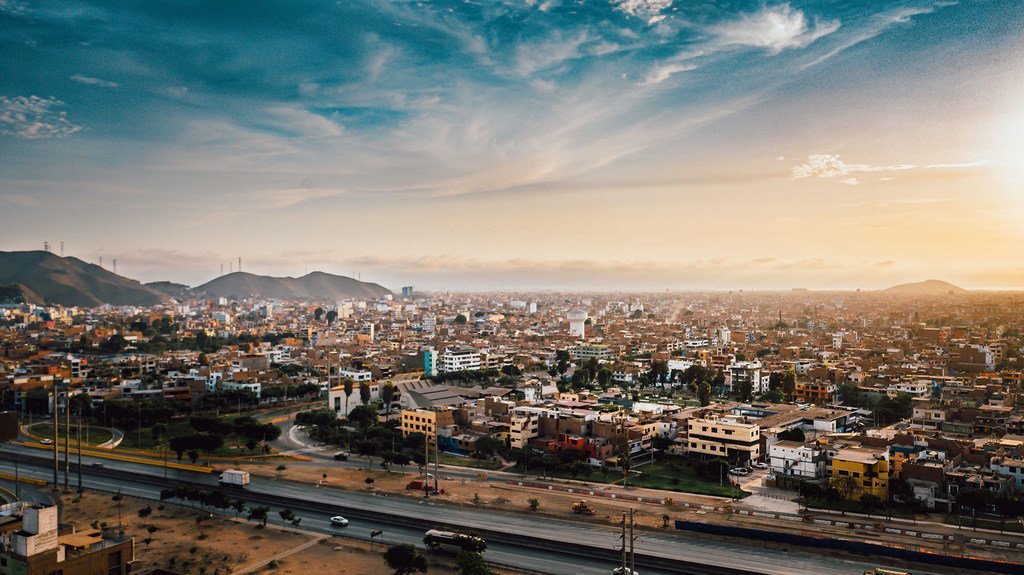 Vista aérea de la ciudad de Lima, Perú, al atardecer, con montañas al fondo y una carretera en primer plano.