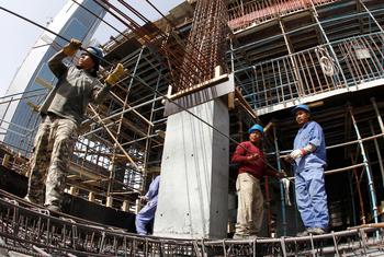 عمال مهاجرون ينقلون قضبان معدنية في ورشة بناء في قطر.