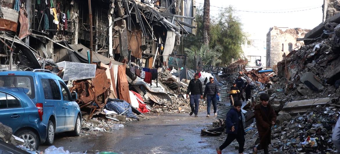 गाजा में लोग विनाशकारी घरों और मलबे से भरी एक सड़क से गुजर रहे हैं, जिससे नागरिकों की सुरक्षा के लिए जारी खतरे पर प्रकाश डाला जा रहा है।