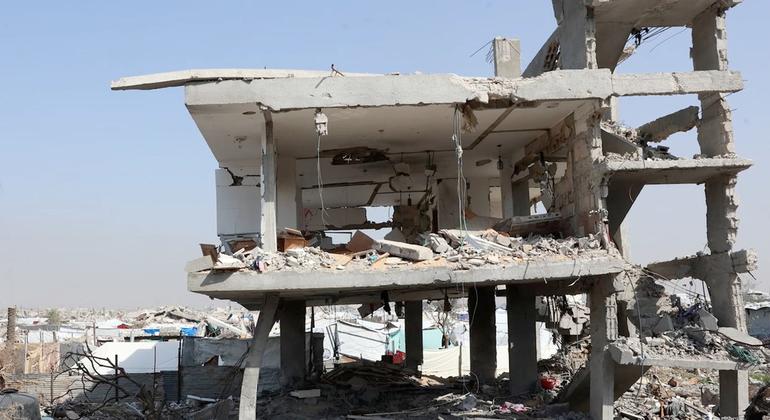 Серьезно поврежденное многоэтажное здание находится на фоне широкомасштабных разрушений в Газе, что подчеркивает опасность, с которой сталкиваются перемещенные семьи, укрывающиеся поблизости.