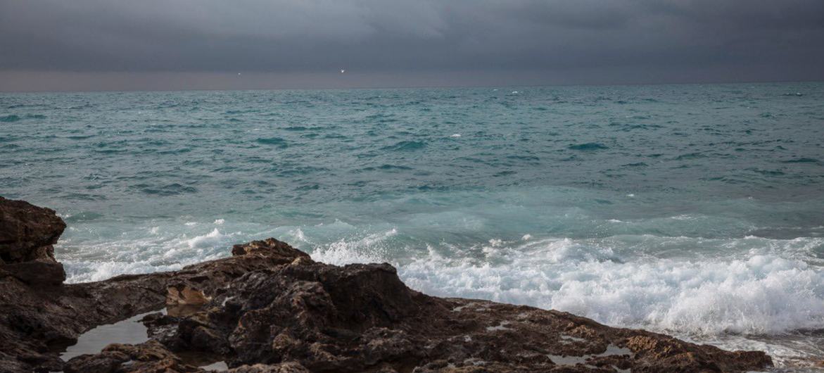 Les vagues s'écrasent contre un littoral rocheux en Libye, sous un ciel sombre et nuageux qui recouvre la mer Méditerranée.