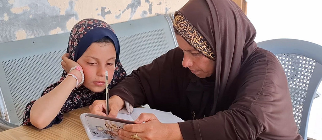 امرأة فلسطينية تُدرّس فتاة صغيرة في فصل دراسي.