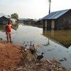 Mtoto akiwa juu ya lundo la mchanga ambao hutumiwa na wakazi wa eneo hili kujaribu kuzuia maji ya ziwa Albert yasiingie kwenye makazi yao.