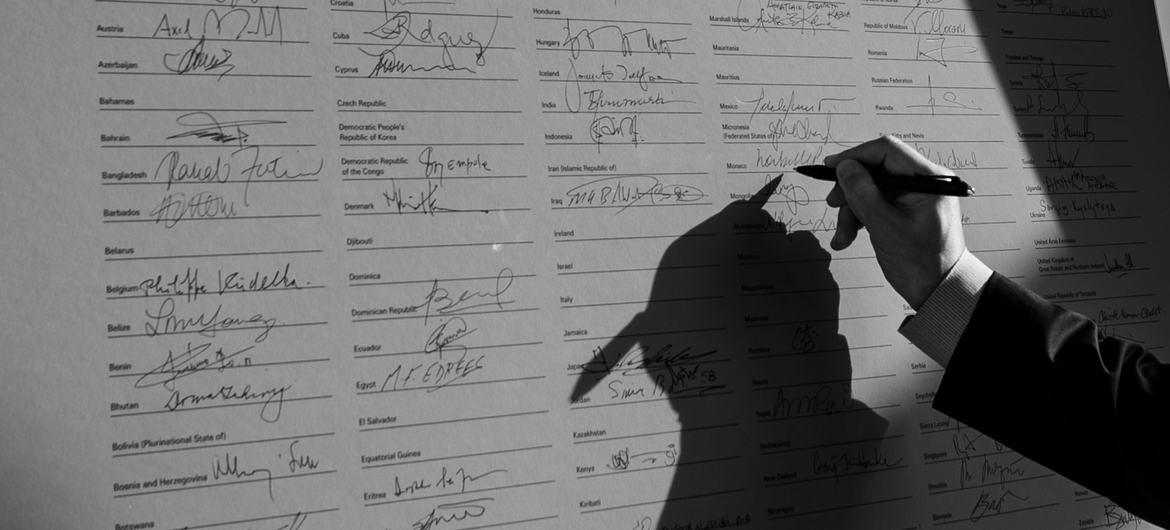 Une main tenant un stylo signe le préambule de la Charte des ONU lors d'une cérémonie commémorative.