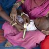 Mfanyakazi wa afya anapima mzingo wa katikati ya mkono wa juu wa mtoto mchanga anayeshikiliwa na mwanamke katika kliniki nchini Sudan.