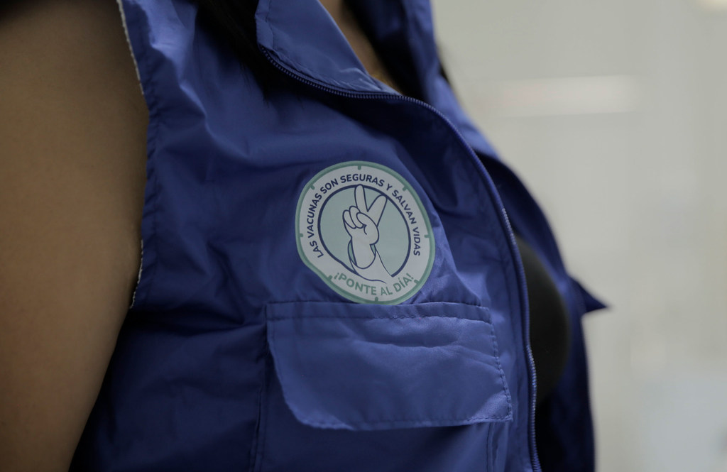 Primer plano de una persona con un chaleco azul con el logotipo de la campaña de vacunación de Paho.