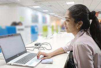 बालों की पोनीटेल बनाए एक दक्षिण एशियाई महिला आधुनिक कार्यालय के माहौल में लैपटॉप पर काम कर रही है।