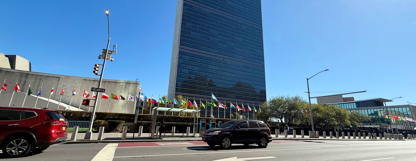 Le bâtiment du Secrétariat des Nations unies à New York, avec les drapeaux des États membres en premier plan sous un ciel bleu éclatant.