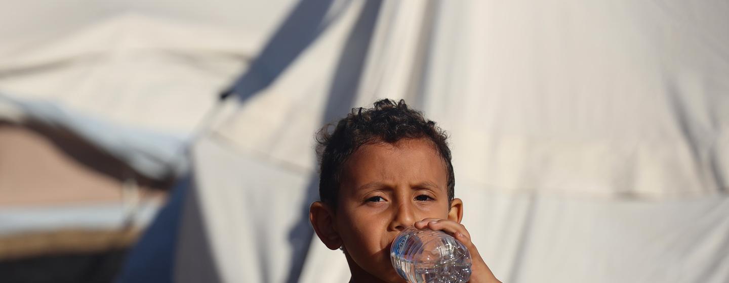 在加沙汗尤尼斯流离失所者营地，一名五岁男孩在喝儿基会提供的瓶装水。