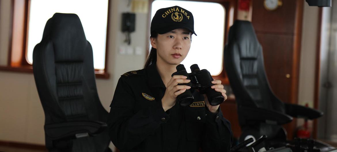 Uma marinheira chinesa, vestindo uniforme da Marinha Mercante da China (China MSA), segura binóculos na ponte de comando de um navio.