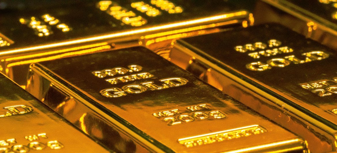 Uma visão aproximada de várias barras de ouro empilhadas, com as inscrições '999.9 GOLD' e 'NET WT 1000g' estampadas na superfície.