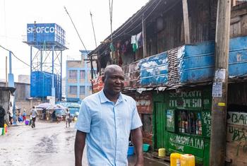 Kennedy Odede akitembea katika mitaa ya Kibera tanki la maji la kujenga SHOFCO likiwa nyuma yake.