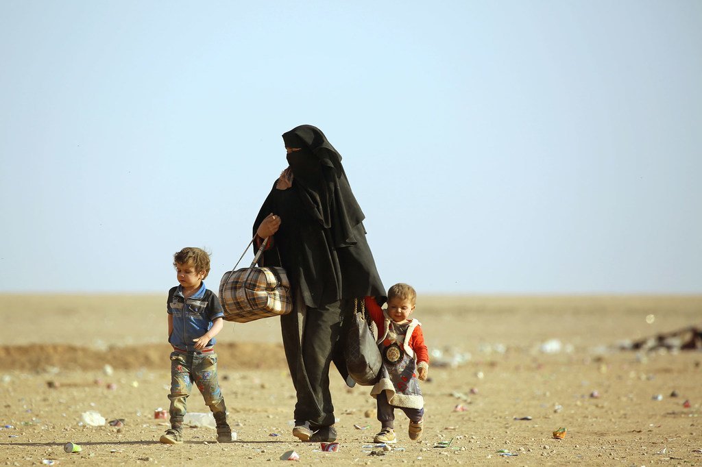 امرأة ترتدي النقاب تسير مع طفلين صغيرين عبر أرض قاحلة.