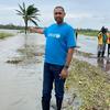 Claudio Julaia está em uma área alagada, apontando para o terreno inundado com uma equipe da Unicef ao fundo.