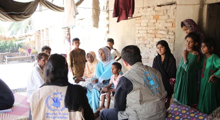 سیلاب سے متاثرہ ایک خاندان خوراک کے حصول اور موسم کی آئندہ صورتحال جاننے کے لیے ڈبلیو ایف پی کے عملے کے گرد ایک امدادی مرکز پر اکٹھا ہے۔