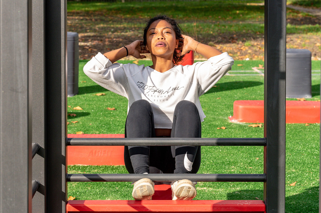 Una mujer realiza abdominales en un aparato de gimnasia al aire libre en un parque.