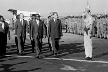 UN Secretary-General Dag Hammarskjöld, Premier Cyrille Adoula, and Dr. Sture Linner walk on an airport tarmac past a Guard of Honor.