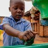 Mtoto mchanga mweusi aliyevaa sare ya shule ya bluu anaosha mikono yake kwenye bomba la maji la kijani katika Kituo cha Maendeleo ya Watoto Wadogo cha Gikomero nchini Rwanda.