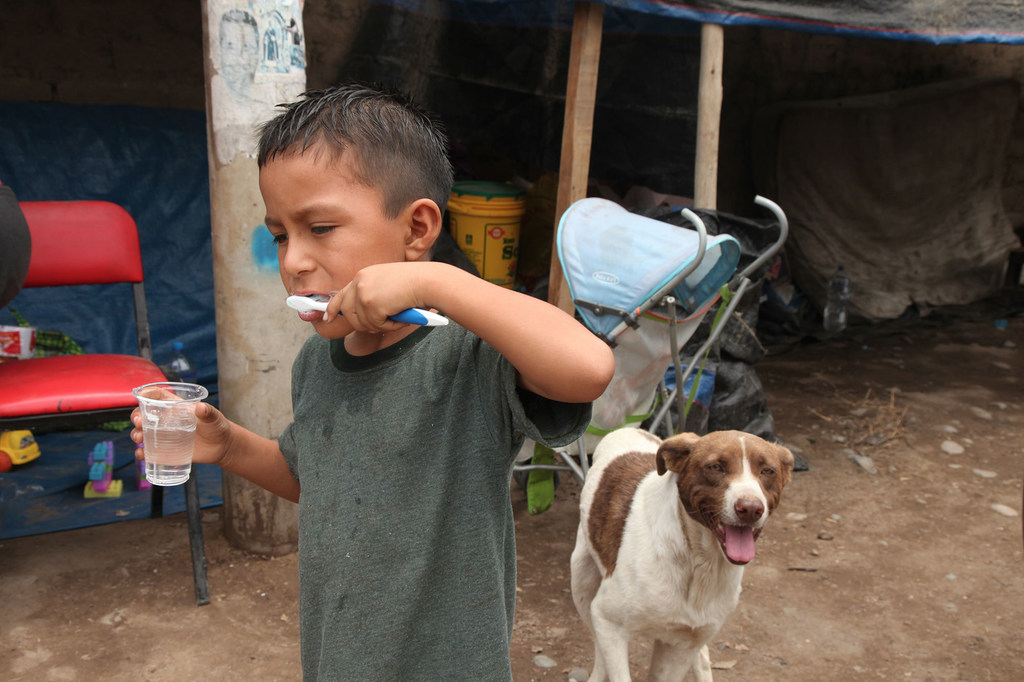 طفل نازح دمر منزله الفيضانات ينظف أسنانه خارج ملجأ مؤقت في ليما، بيرو.