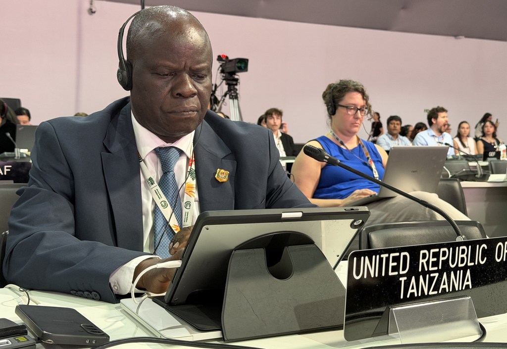 Dkt. Richard Muyungi, Mjumbe Maalum wa Mabadiliko ya Tabianchi kutoka Tanzania, ameketi kwenye meza ya mkutano akiwa na bango la 'JAMHURI YA MUUNGANO WA TANZANIA' wakati wa mkutano wa kilele wa COP30 huko Belem, Brazil.