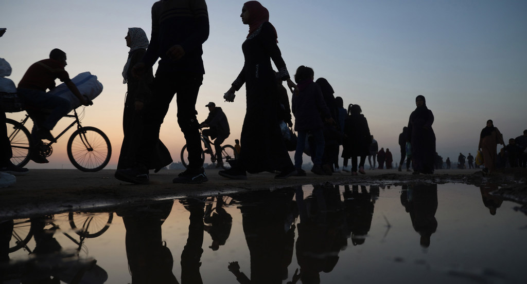 صور ظلية لأشخاص نازحين، بمن فيهم نساء وأطفال، يسيرون بالدراجات الهوائية ويحملون المؤن عند الغسق في غزة.