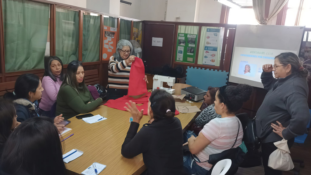 Una anciana muestra un proyecto de costura a un grupo de mujeres en un centro comunitario de Argentina.