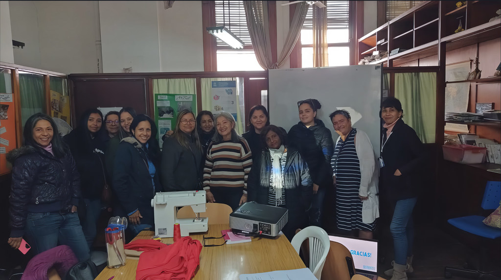 Un grupo de mujeres, entre ellas Gladis, una refugiada venezolana de 71 años, se reunieron en un taller en Argentina. Sobre la mesa, frente a ellas, hay una máquina de coser.