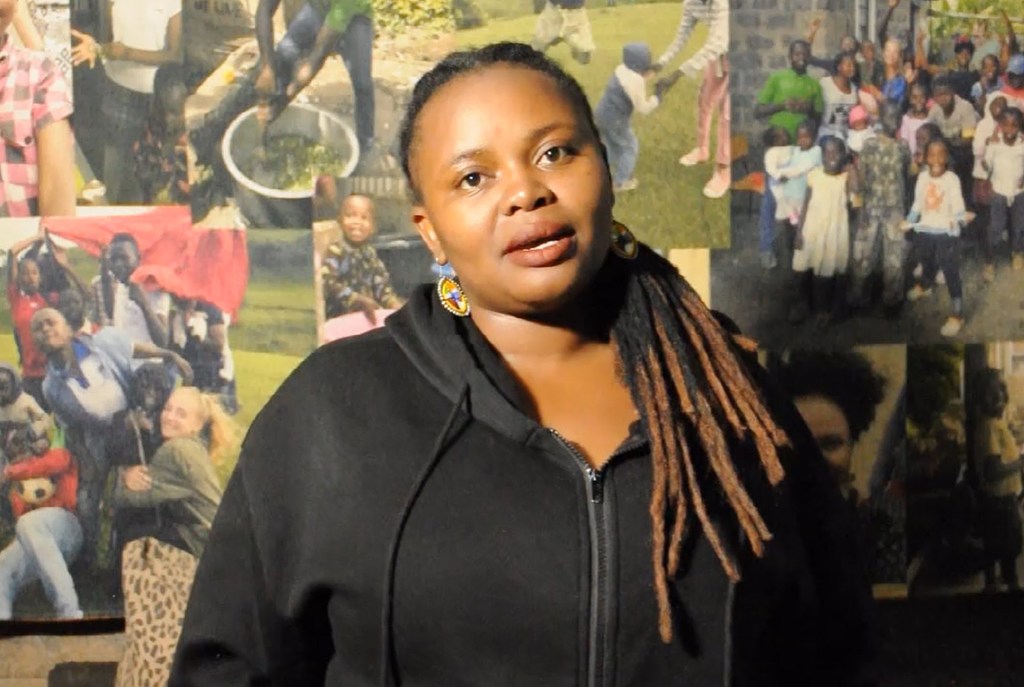 Mary Anne Mwangi, Naibu Mwanzilishi wa Kituo cha Watoto cha Priscilla and Angelica Chalks Foundation, amesimama mbele ya ukuta wa kolagi huko Embulbul, Kaunti ya Kajiado.