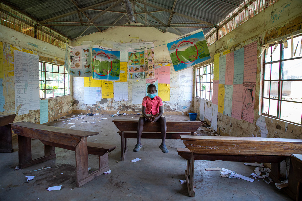 On iki yaşında bir erkek çocuk, COVID-19 salgını sırasında kapatılan bir okulun boş sınıfında oturuyor.