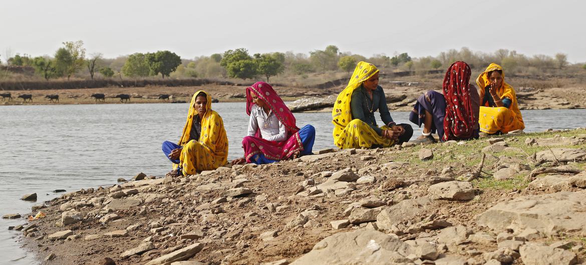 भारत के राजस्थान में एक पथरीले नदी किनारे पर रंग-बिरंगी साड़ियों में सजी पांच महिलाएं बैठी हैं।