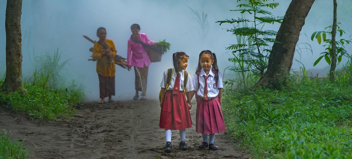Two young schoolgirls walk through a forest in Indonesia.
