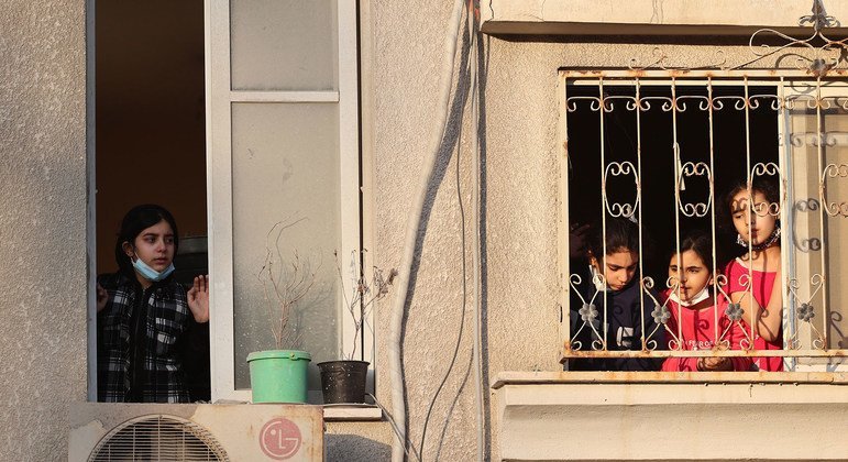 फ़लस्तीनी बच्चे अपनी खिड़की से बाहर क्षतिग्रस्त इमारतों को देखते हुए.