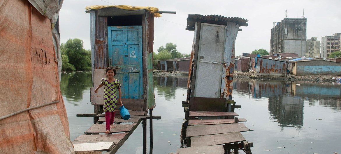 فتاة صغيرة تخرج من مرحاض تم تشييده على ركائز متينة حيث يتم إطلاق النفايات مباشرة في مصدر مياه مفتوح في مومباي، الهند.