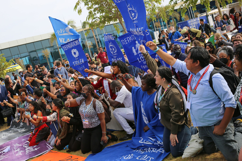 A diverse group of indigenous peoples, environmental activists, and youth raise their fists in solidarity during the COP27 Peoples' Plenary in Egypt.