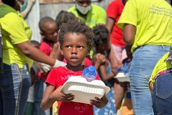 Un jeune enfant haïtien tient un récipient pour son repas et une bouteille d'eau lors d'une distribution du Programme alimentaire mondial en Haïti.
