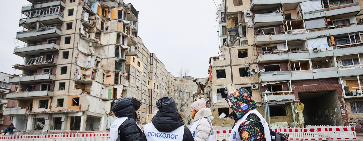 Psicólogos de crise, trajando coletes brancos, estão perto de um prédio de apartamentos destruído em Dnipro, na Ucrânia.