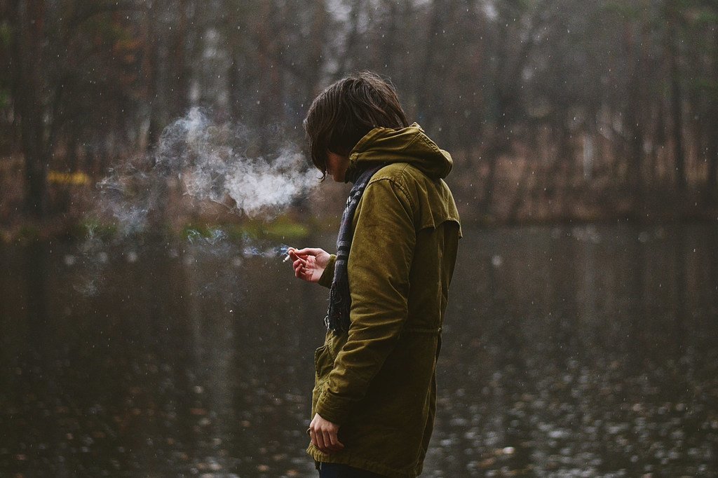 Un jeune homme fume une cigarette.