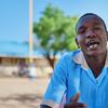 Mvulana mdogo mkimbizi aliyevaa sare ya shule akizungumza akiwa ameketi nje ya jengo la shule huko Kakuma, Kenya.