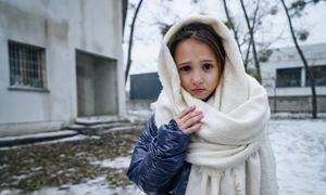 An 8-year-old girl poses in front of a building in Irpin, Ukraine where her mother and sister share a small room.