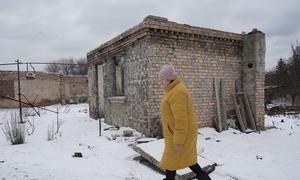 Uma mulher passa por sua casa danificada na vila de Horenka, no Oblast de Kiev