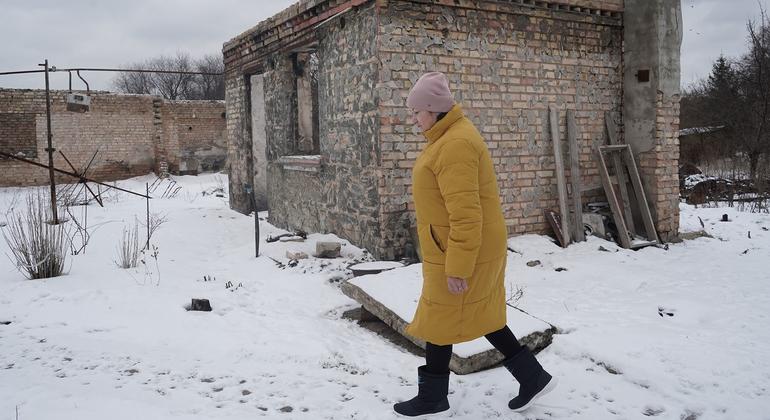 Uma mulher passa por sua casa danificada na vila de Horenka, no Oblast de Kiev